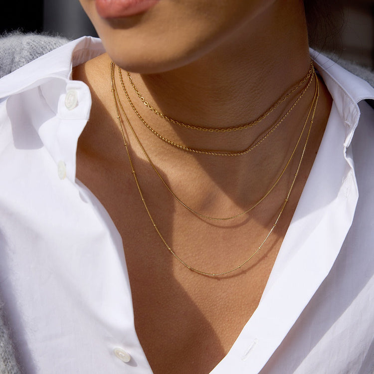 woman dress in brown shirt posing on necklace on that has rose and pearls