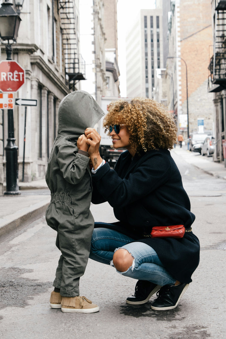 Woman bending down holding onto her toddler hands smiling 