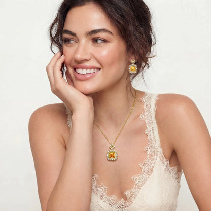 Woman wearing a gold necklace and earrings with a white lace top on a light background