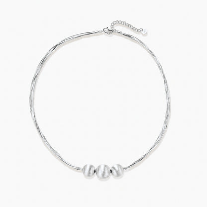 Sterling silver multi-strand necklace with three brushed round beads on cream background
