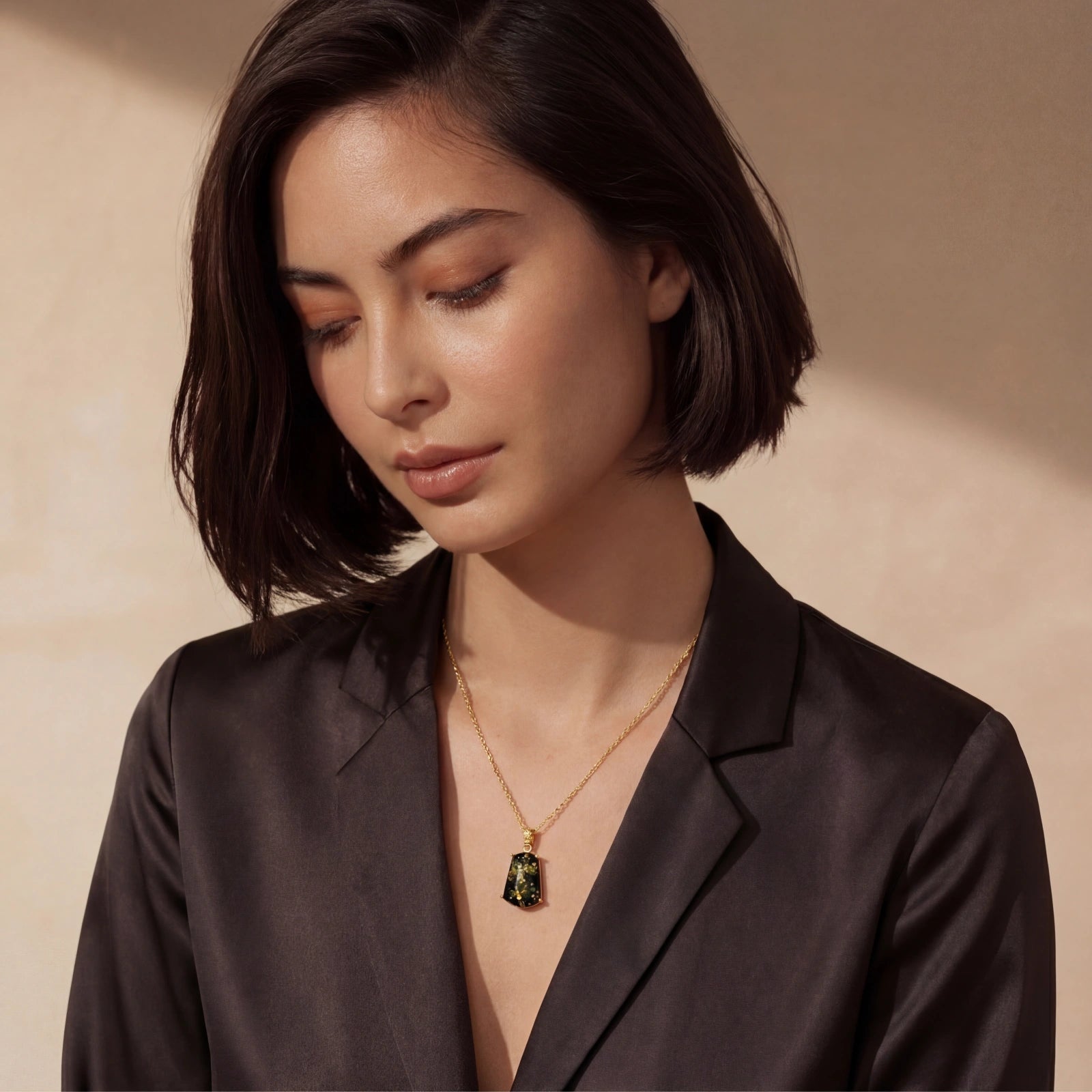 Woman wearing a black blazer with a gold necklace against a beige background