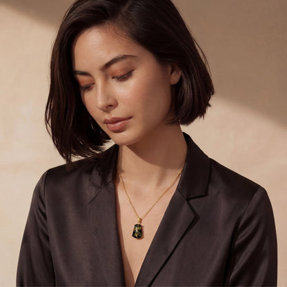 Woman wearing a black blazer with a gold necklace against a beige background