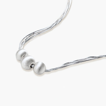 Sterling silver multi-strand necklace with three brushed round beads on cream background