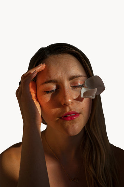 Woman applying a patch to her face against a dark background